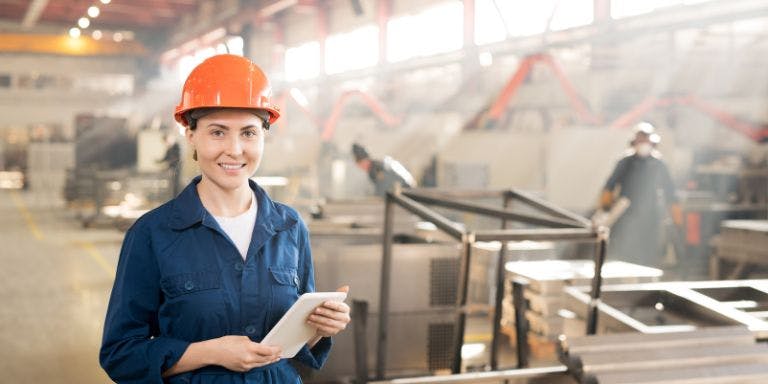 A woman in a hard hat uses a tablet to assess workplace exposure limits in a safety-focused setting.