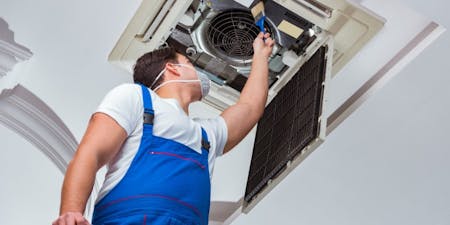 Workplace exposure limits A man in blue overalls repairs an air conditioner, demonstrating workplace safety and adherence to exposure limits.