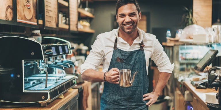 Staggered hours A happy man in an apron smiles while holding a cup, representing a business owner thriving with flexible work hours.
