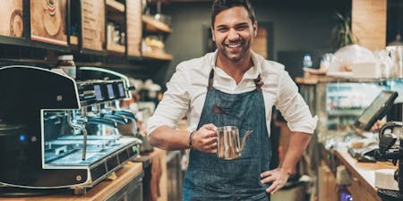 Staggered hours A happy man in an apron smiles while holding a cup, representing a business owner thriving with flexible work hours.