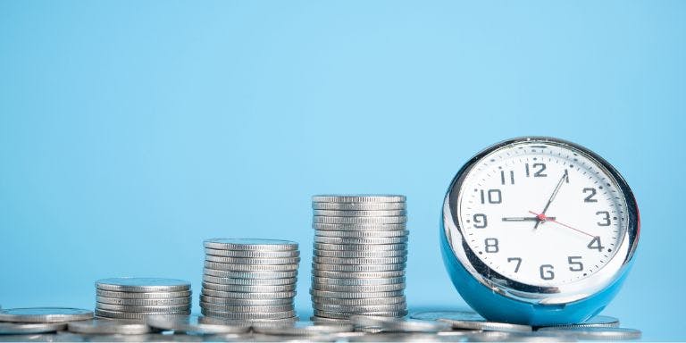A clock sitting on a pile of coins to indicate time equals money