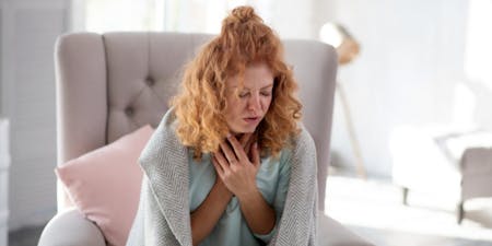 Managing sickness at work Woman on a chair in bedroom holding her chest and coughing.