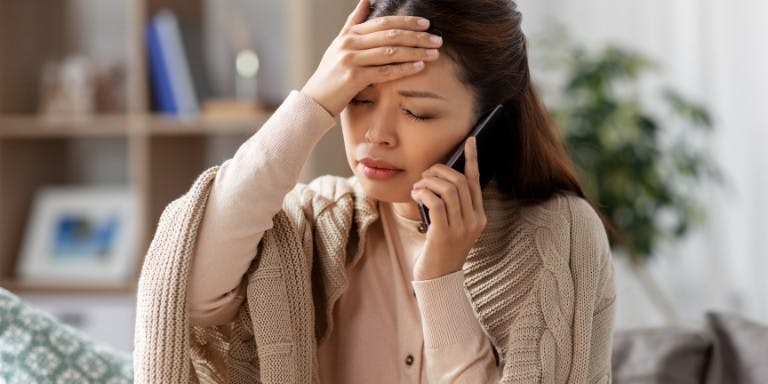 Sick leave in Canada Sick female employee on the phone with hand on head.