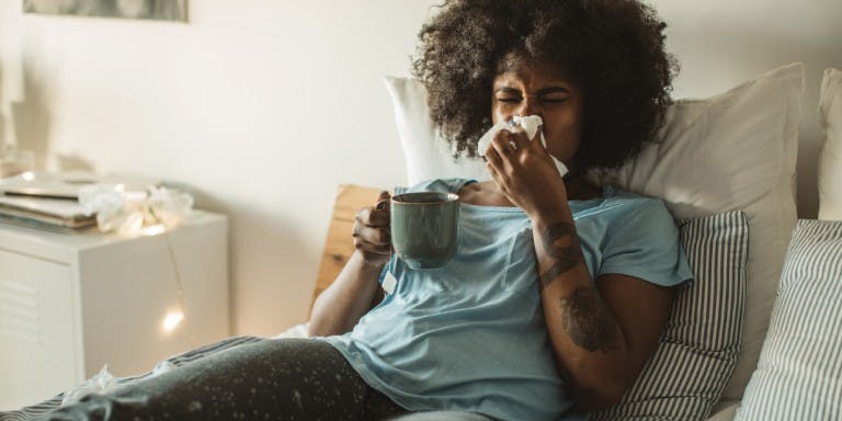 Women on sick leave in bed with a cup of tea and blowing nose.