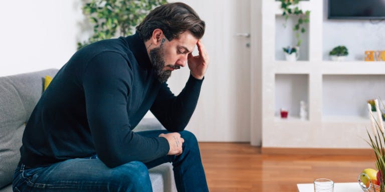 Man sitting on a couch with his head in his hands, reflecting on his mental health during sick leave.