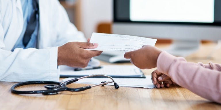 A doctor handing over a fit note to a person over a table.