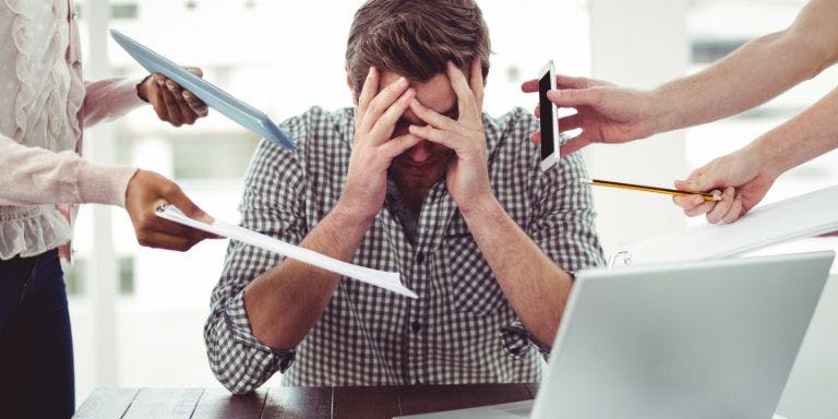 Male employee with hand on head stressed with many people coming up to him
