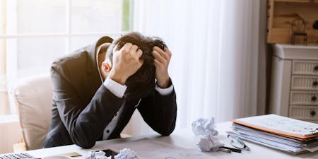 Man at desk looking stressed with loads of paperwork around him