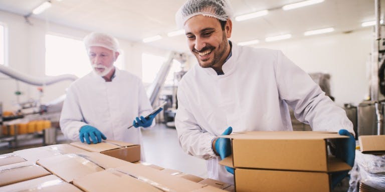 Two men in a food packing facility packing up prepared meals