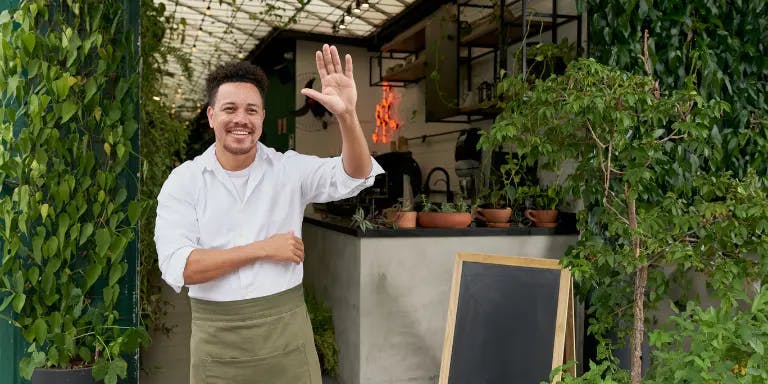 A man standing outside a plant shop smiling and waving