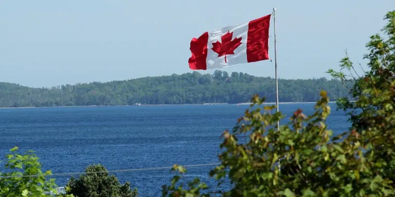 Canada flag waving in the wind with a lake in the backgroun