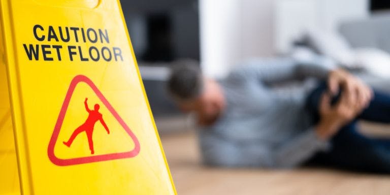 Slips, trips and falls in the workplace A wet floor sign with a man who has fallen in the background