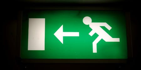 Safe condition signs in the workplace A fire exit sign lit up in green and white lights to hihglight the designated escape route and emergency exit