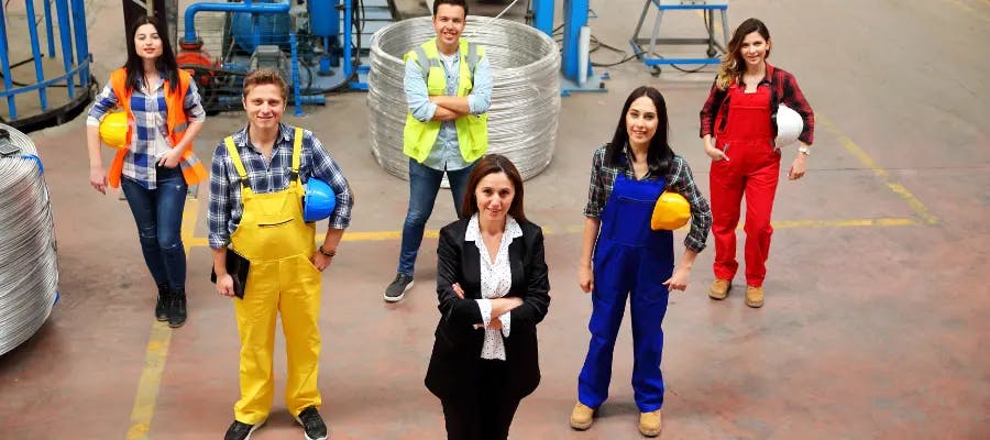 6 workers standing in a v formation. 4 of them have hard hats tucked under their arms.