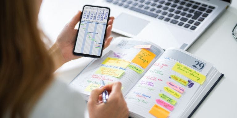 A small business owner scheduling employee shifts manually using a calendar and diary