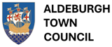 The image features a blue shield with a white border, on which a ship is depicted. The ship is adorned with red and white flags, and the ship's sails are white with red and blue stripes. The ship is sailing on a blue sea, with white waves surrounding it. The ship's design is symmetrical, with the sails and the ship aligned in a diagonal line. The shield and the ship are the main elements in the image, with the background being a stark black. The ship appears