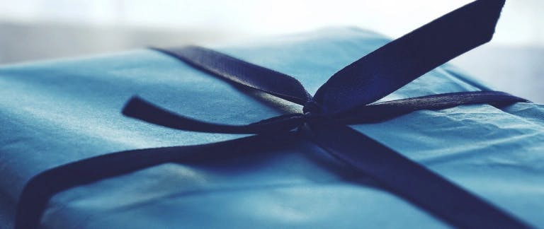 A present gift-wrapped in plain blue paper with a navy ribbon tied around it