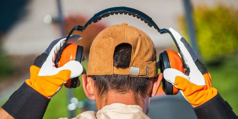 A construction worker placing ear defenders on their head and over their ears