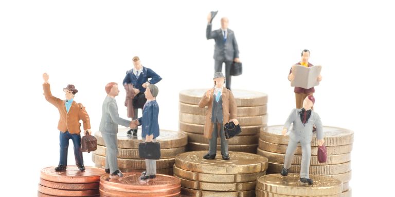 A miniature group of business people are gathered atop a pile of gold coins. The coins are arranged in a pyramid shape, with the topmost coin being the largest and the bottommost coin being the smallest. The people in the group are dressed in business attire, with some holding briefcases and others carrying suitcases. They are standing on the coins, with some of them raising their arms in a gesture of unity or success. The image conveys a sense of unity and success, possibly symbolizing a