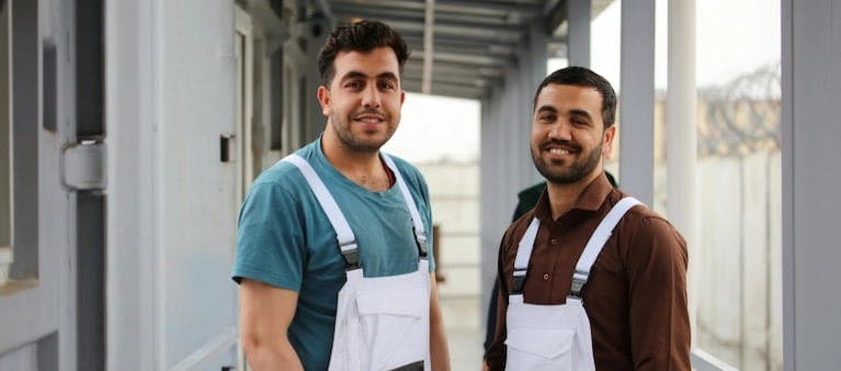 Two workers in overalls stood smiling at the camera
