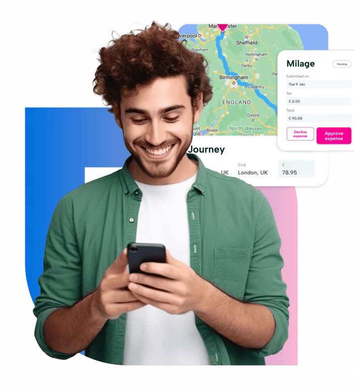 A young man with curly hair is smiling while looking at his phone. He is wearing a green shirt and is standing in front of a map of the United Kingdom. The map is displayed on a screen with a blue background and a white border. The man is holding a black phone in his hands.