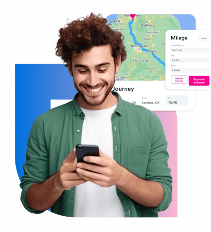 A young man with curly hair is smiling while looking at his phone. He is wearing a green shirt and is standing in front of a map of the United Kingdom. The map is displayed on a screen with a blue background and a white border. The man is holding a black phone in his hands.