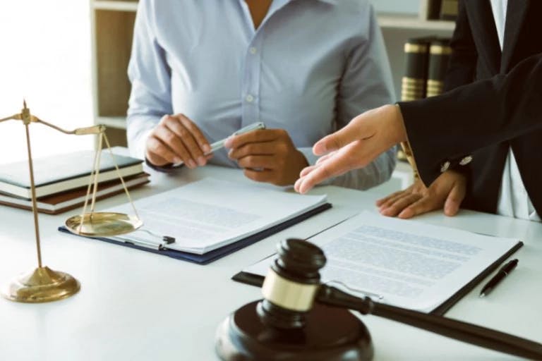 In a well-lit room, two individuals are seated at a desk, engaged in a legal or business context. The person on the left is holding a pen, poised to sign a document, while the person on the right is holding a gavel, a tool used in legal proceedings. The desk is adorned with various documents and books, suggesting a formal setting. The background features a bookshelf filled with books, indicating a knowledge-rich environment. The overall scene conveys a sense of professionalism and dedication In a well-lit room, two individuals are seated at a desk, engaged in a legal or business context. The person on the left is holding a pen, poised to sign a document, while the person on the right is holding a gavel, a tool used in legal proceedings. The desk is adorned with various documents and books, suggesting a formal setting. The background features a bookshelf filled with books, indicating a knowledge-rich environment. The overall scene conveys a sense of professionalism and dedication