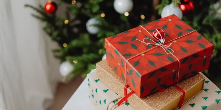 A festive scene with a stack of wrapped presents, a decorated Christmas tree, and a white table.