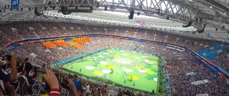 A photograph of a football pitch in a stadium with cheering crowds