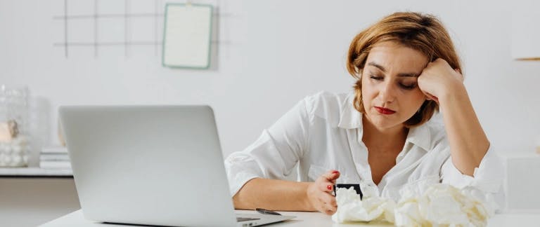 A woman sitting behind a laptop with a pile of tissues next to her