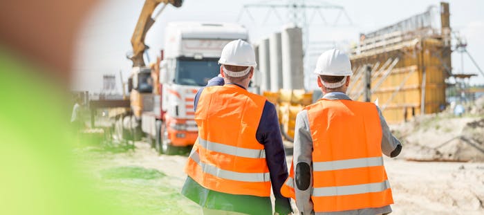 An image showing two construction workers allowing the entrance of a HGV onto the site