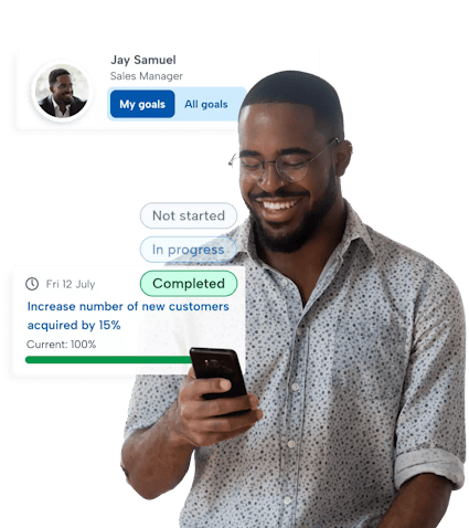 Performance management software A man looking down smiling at his phone using BrightHR's performance management software to complete a goal