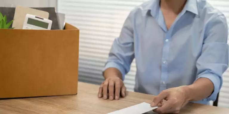 An image of a man receiving a letter of dismissal with a box of items on his desk