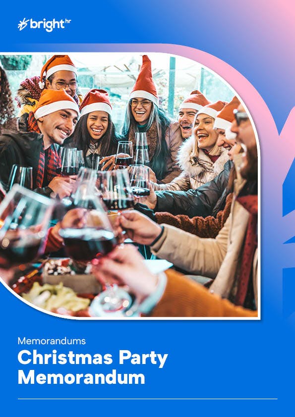 A group of people are gathered around a table, all wearing Santa hats, and are holding wine glasses filled with red wine. The atmosphere appears festive and joyful.