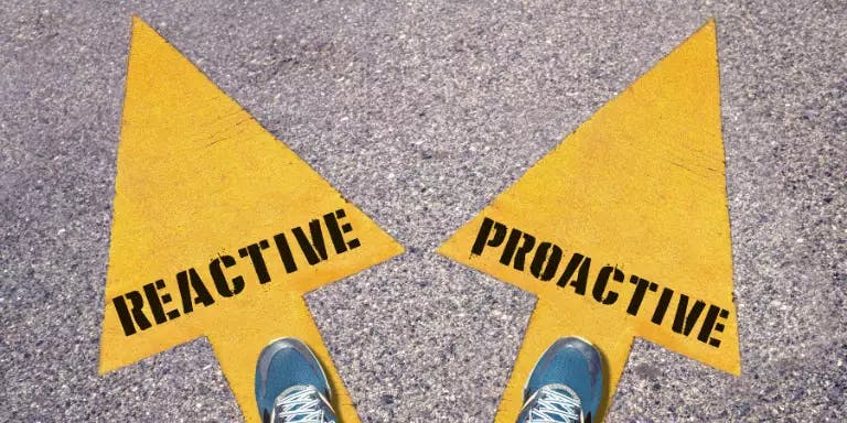A person standing on two yellow arrows. One has the word Reactive painted on it while the other says Proactive