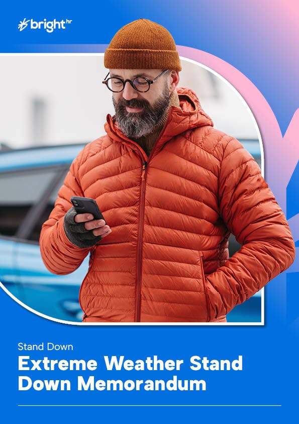 A man wearing an orange beanie and a red winter coat is standing in front of a blue car. He is holding a black phone in his right hand