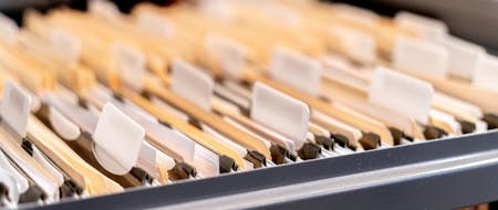 A photograph of a filing cabinet drawer with paper files inside