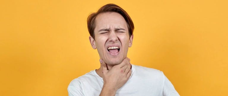 Sore throats and sickness A person standing in front of a yellow background holding their throat and grimacing