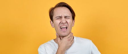Sore throats and sickness A person standing in front of a yellow background holding their throat and grimacing
