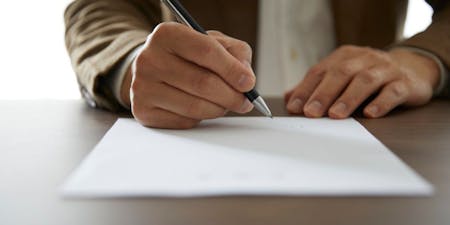 Shot of a desk with a person signing a document by pen