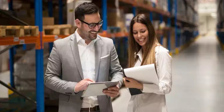 Two people walking through a warehouse holding tablets and notepads