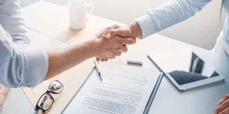 Interim relief application and agreement Two people shaking hands over a desk to make an agreement