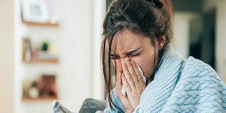 Employee taking sick leave A person sneezing into a tissue on the sofa in their home due to a workplace sickness