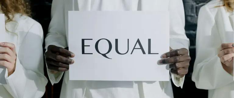 three people dressed in white standing next to each other. the person standing in the middle is holding a sign that says 'equal' in black three people dressed in white standing next to each other. the person standing in the middle is holding a sign that says 'equal' in black