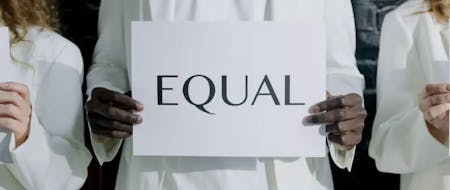 three people dressed in white standing next to each other. the person standing in the middle is holding a sign that says 'equal' in black three people dressed in white standing next to each other. the person standing in the middle is holding a sign that says 'equal' in black