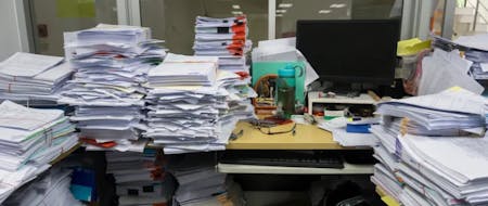 A messy office desk covered in piles of paper and files