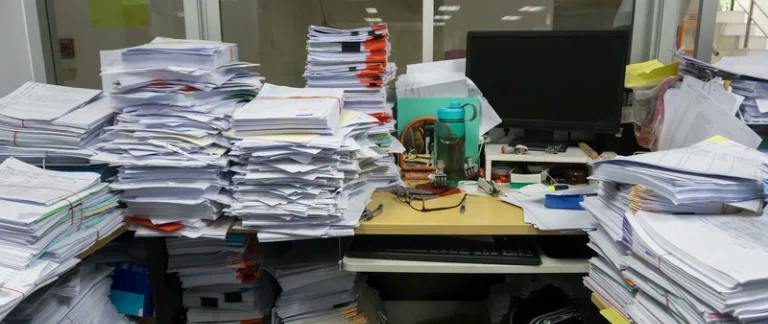A messy office desk covered in piles of paper and files