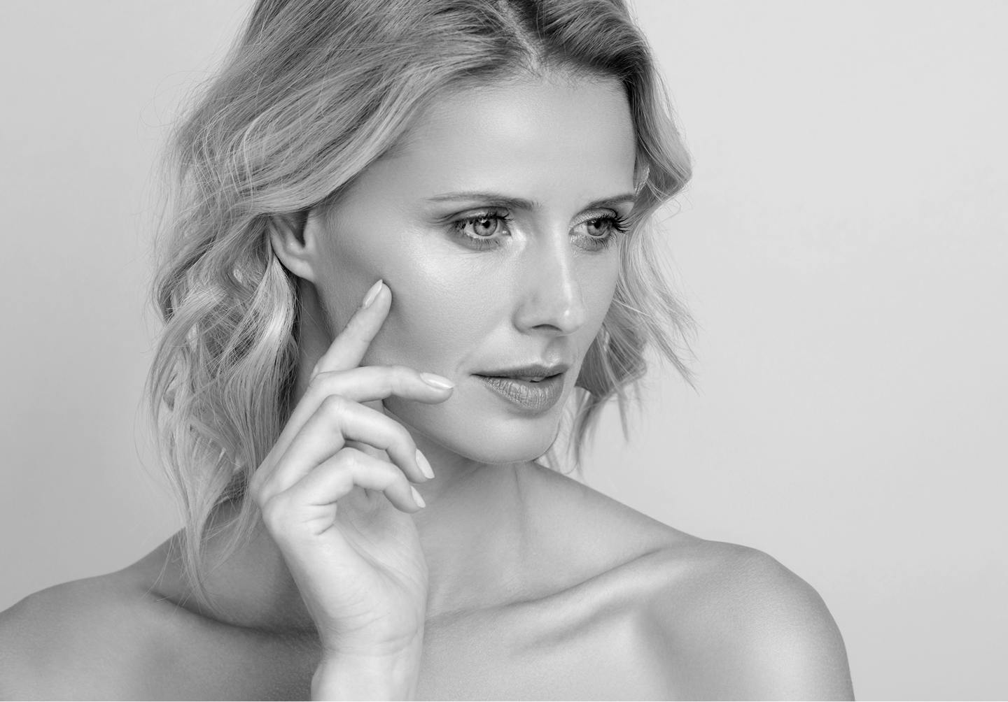 Black and white photo of a model with bare shoulders and her hand on her face.