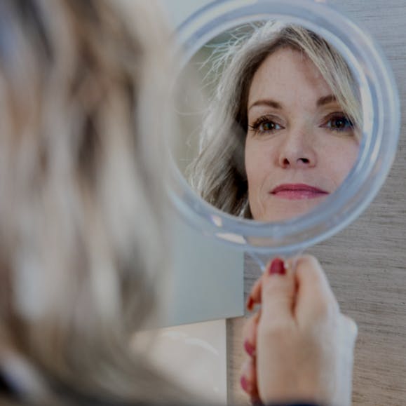 Woman looking in a handheld mirror.