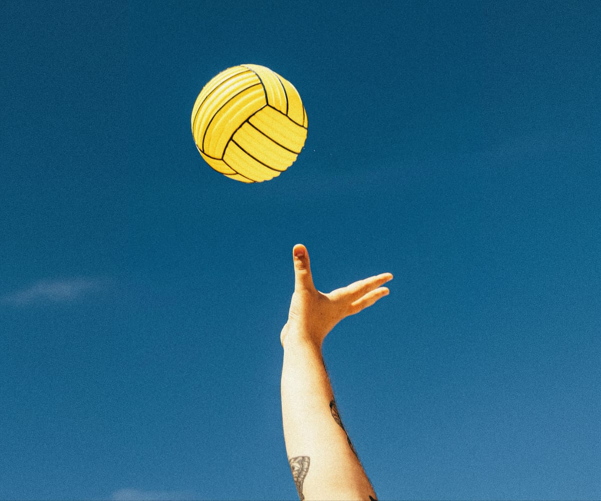 Hand reaching for a yellow ball against a blue sky
